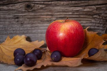 apple, grapes and yellow autumn leafs on old textured wood background