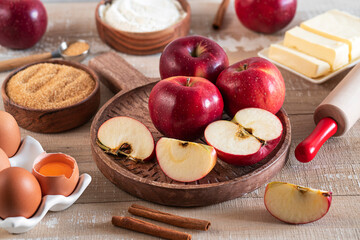 Close-up of ingredients for Apple pie or Charlotte. Ingredients for apple pie - red apples, flour, eggs, sugar, cinnamon and butter on a wooden table