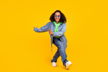 Fototapeta na wymiar Photo of beautiful funky african lady dressed jeans green hoodie dark eyewear dancing smiling isolated yellow color background