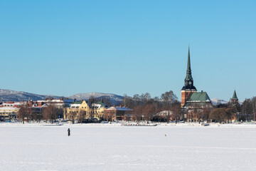 person walking a dog on a frozen lake in a small town in winter in the snow, in Mora (Dalarna) Sweden