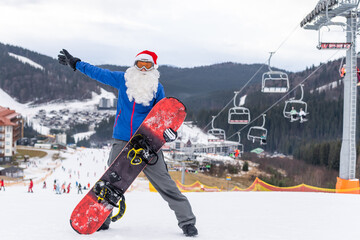 happy man in santa red christmas hat with snowboard at winter mountains hill