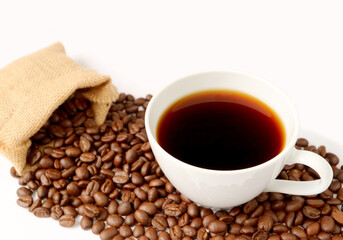 A cup of hot coffee with roasted coffee beans scattered from burlap bag