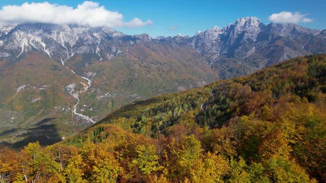 Panoramic cinematic shot of Autumn scene with yellow-red trees and mountains in sunlight