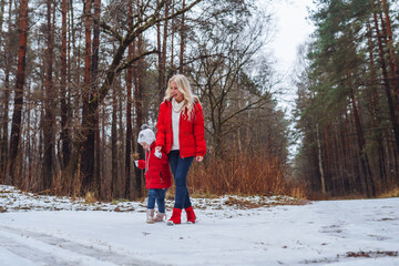 Family of mother and daughter dressed in red clothes walk in winter snowy forest. Females have fun and spend time together.