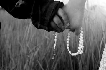 Two kids holding hands with Rosary in hands in monochrome black and white backgrounds. Children...