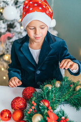Santa little helper with decorative christmas tree on background. Little smiling boy make christmas...