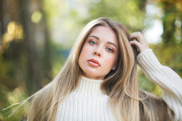 beautiful fashionable young girl in a white sweater in the park among the trees, caucasian girl...