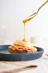 egg Benedict with hollandaise sauce on blue plate on table in white kitchen