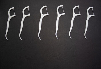 set of plastic white dental toothpicks in a row line isolated on black background.woman hand holding one sticks or a lot of dental floss arranged chaotic. dental floss,oral hygiene daily routine care.