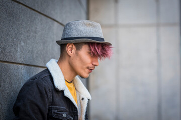 Serious and trendy alternative look style teenager male with violet hair and hat posing against a...