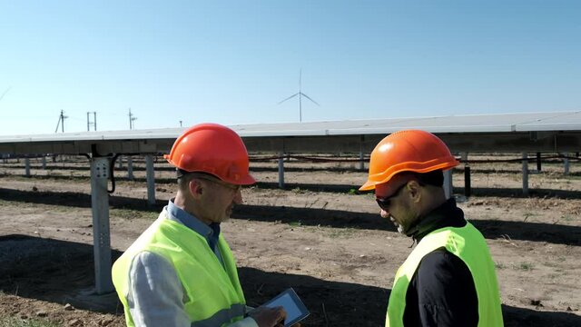 Solar wind energy workers at farm. Safety engineer gives instructions to employee with sunglasses at construction site of electrical substation