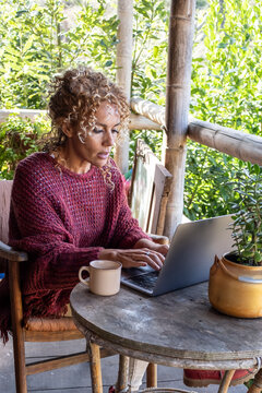 Modern adult woman work outdoor with laptop computer sitting on the table with nature trees background. Female caucasian people busy in online job internet activity outside