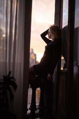 Beautiful young woman near the window on sunset. City view