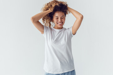 Obraz na płótnie Canvas Smiling woman with lush curly hair in white blank t-shirt on a white background. Mock-up.