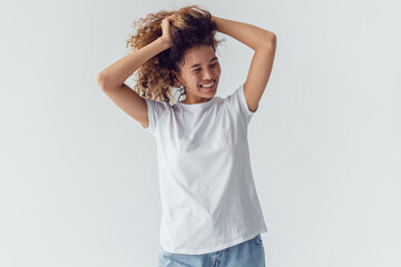 Fototapeta premium Smiling woman with lush curly hair in white blank t-shirt on a white background. Mock-up.