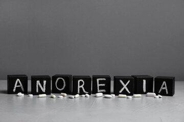 Word Anorexia made of cubes with chalked letters near pills on light table