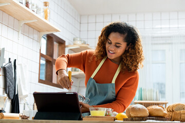 Young African American woman teaching cooking and broadcasting online via tablet computer in kitchen at home