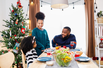 African American family surprising together with a gift on Christmas day while dinner. Merry Christmas. Happy family.