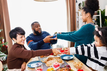 African American family surprising together with a gift on Christmas day while dinner. Merry Christmas. Happy family.
