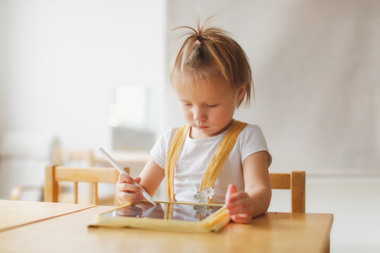 Funny cute baby girl toddler with tablet, child and gadget. Early development and drawing on the screen, the child plays and learns on the tablet