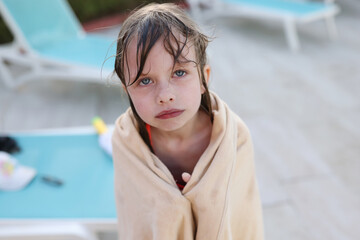 Little frozen girl in towel standing near swimming pool