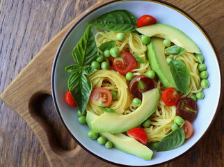 Pasta salad with green peas, avocado, cherry tomatoes and basil on rustic wooden background. Top view