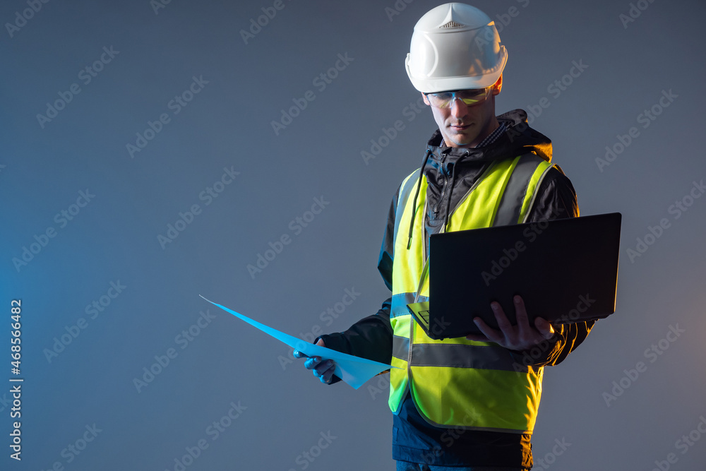 Poster builder-architect looks at laptop. portrait of man in construction uniform. architect in yellow vest
