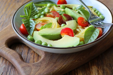 Pasta salad with green peas, avocado, cherry tomatoes and basil on rustic wooden background. Top view