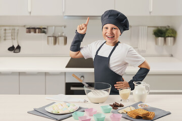 The boy in the cook's uniform smiles and holds his finger up. Preparation of cream, ice cream. Modern white kitchen. Dessert, chocolate,milk, towels, silicone molds whisk