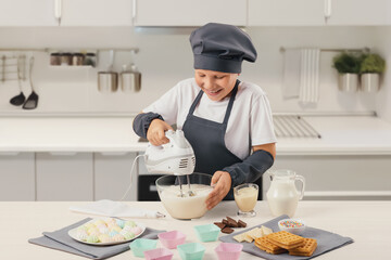 The child prepares ice cream, cream. Apron and cap. He holds a mixer in his hand and whips cream in...