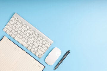 Top view office desk with keyboard, pen, mouse, and notebook. Blue table with the gadget for business put on the table neat. Empty blue background copy space.