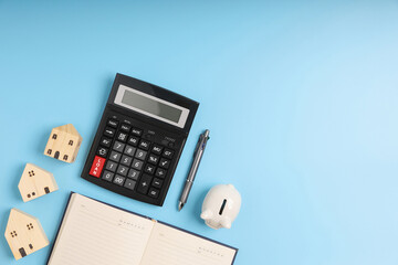 Top view LOAN on the black calculator with little home models, notebook, and white piggy bank on blue background with copy space. Concept saving money for investment business property.