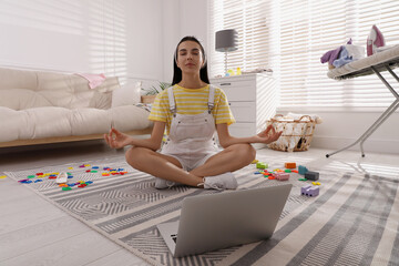 Calm young mother meditating on floor in messy living room