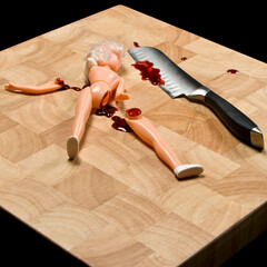 Childs doll with leg chopped off, bleeding, with knife on chopping block