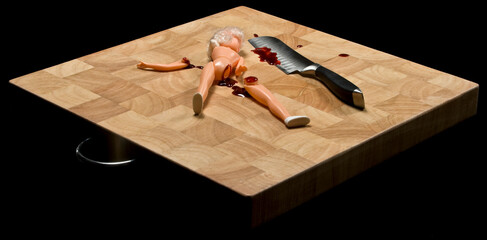 Childs doll with leg chopped off, bleeding, with knife on chopping block