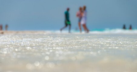 Blured image of unrecognizable people having fun on beach with shimmering water