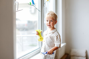 Cute boy toddler blond toddler at the window washes the glass. Helping children with household chores and household chores, children's independence, Montessori classes for small
