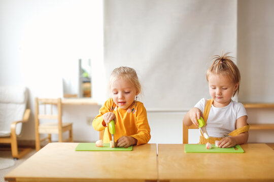 Cute kids toddlers girls at the table cut apples with safe knives, children cut food themselves, montessori and independence in kindergarten