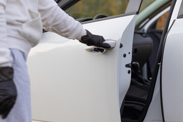 A man in a white sweater and black gloves opens the car door to steal him on a warm autumn day. Selective focus. Close-up