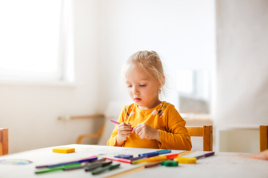 Cute sunny girl child blonde with a ponytail at the table draws with multicolored felt-tip pens, montessori and creativity, creative development in kindergarten