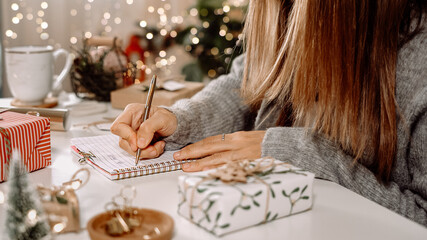 Goals plans make to do and wish list for new year christmas concept, girl writing in notebook. Woman hand holding pen on notepad at home on winter holidays xmas. Christmas decoration, gift boxes. 