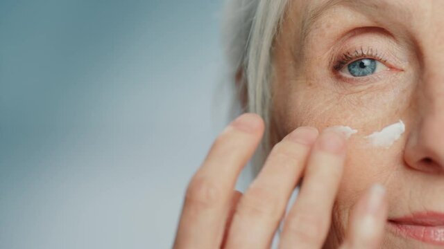 Portrait of Beautiful Senior Woman Gently Applying Under Eye Face Cream. Elderly Lady Makes Skin Soft, Smooth, Wrinkle Free with Natural anti-aging Skincare Cosmetics. Half Face Close-up Stylish Shot