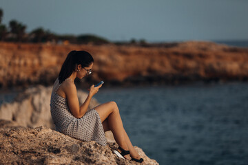 Beautiful young woman on the top of rock near ocean