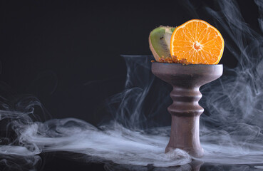 fruit hookah bowl with tobacco, kiwi, tangerine and smoke on black background