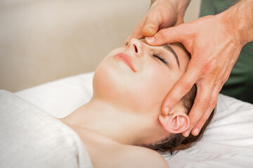 Obraz na płótnie Canvas Pretty young caucasian woman receiving a head massage by a male massage therapist in a beauty salon