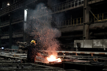 A worker at a metallurgical plant works with red-hot iron. Sparks fly up