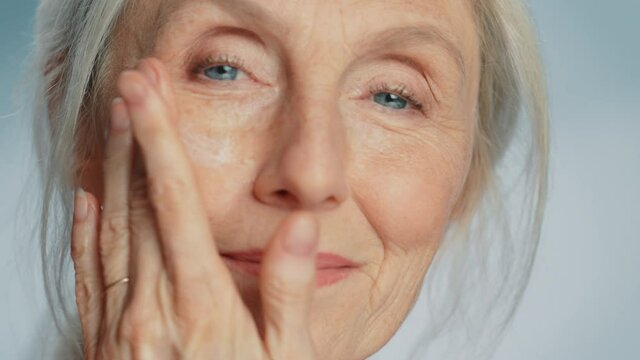 Close-up Portrait of Beautiful Senior Woman Gently Applying Under Eye Face Cream. Elderly Lady Makes Her Skin Soft, Smooth, Wrinkle Free with Natural anti-aging Cosmetics. Product for Beauty Skincare