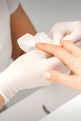 Manicure master wiping the moisturizer from the end of female fingers in beauty salon