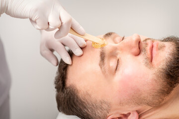 Beautician applying wax paste between eyebrows during the procedure of waxing in the beauty salon - obrazy, fototapety, plakaty
