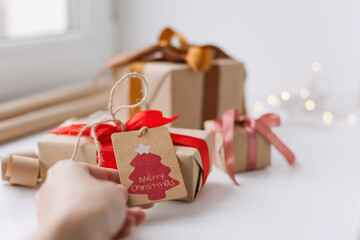 wrapping christmas gifts - hand putting a paper tag on a small gift box with wrapping paper and gifts on background